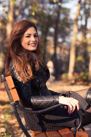 Autumn fashion woman sitting on park bench and smiling with copyspaceの写真素材
