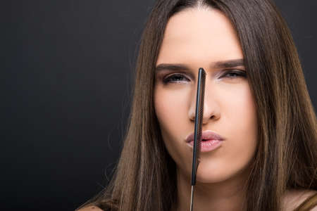 Beautiful sexy woman with straight long hair holding comb on her lips