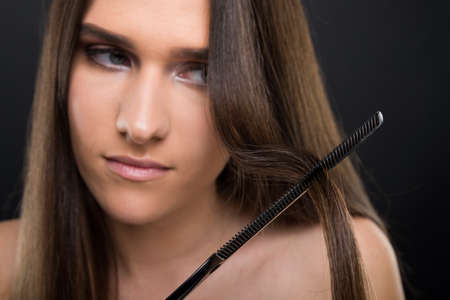 Young woman with smooth skin on dark background combing hair in close-upの写真素材