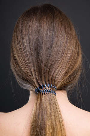 Back view of young woman with ponytail hairstyle in close-up on dark background