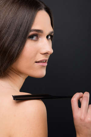 Profile portrait of pure beauty with hair comb posing on dark backgroundの写真素材