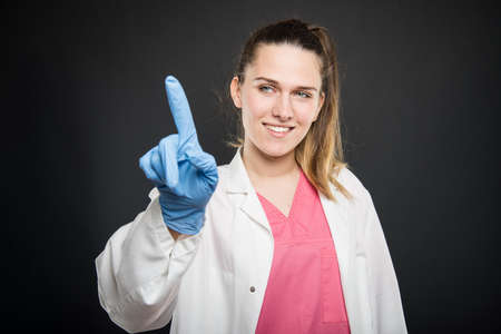 Young doctor portrait wearing robe and scrubs using touchscreen and smiling on black backgroundの写真素材
