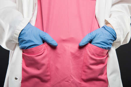Close-up of doctor standing with hands in pockets wearing scrubs and sterile gloves on black backgroundの写真素材