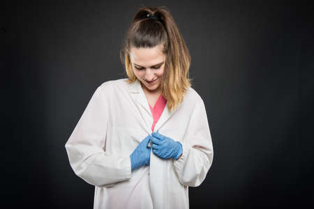 Young female doctor portrait buttoning her white robe on black background with copyspace advertising areaの写真素材