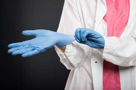 Close-up of doctor putting on her sterile gloves on black backgroundの写真素材