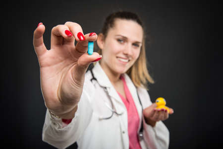 Selective focus of pediatrician doctor holding pill and duck toy on black backgroundの写真素材