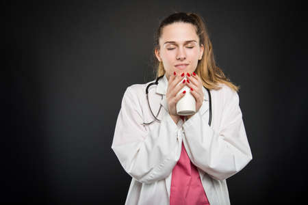 Attractive female doctor enjoying takeaway cup of coffee with eyes closed on black background with copyspace advertising areaの写真素材