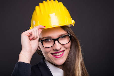 Happy young engineer woman with yellow helmet posing friendly on dark backgroundの写真素材
