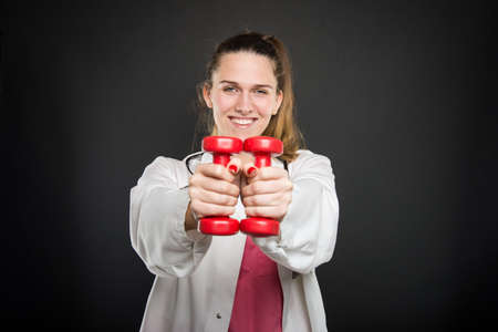 Young doctor portrait  working out with pair of dumbbells and smiling on black backgroundの写真素材
