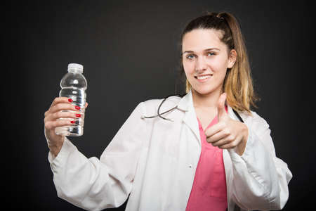 Female nutritionist pointing bottle of water showing like on black backgroundの写真素材