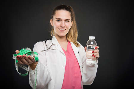 Female doctor portrait  holding measuring tape and bottle of water  on black background with advertising areaの写真素材