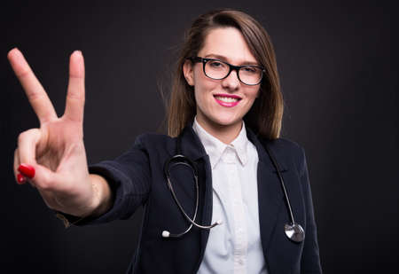 Beautiful female manager showing victory sign and posing with medical stethoscopeの写真素材