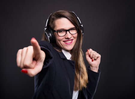Cheerful girl manager pointing you with friendly expression while listening music on headphones