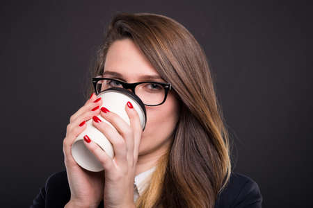Young confident business woman in formal wear drinking coffee to go on dark backgroundの写真素材