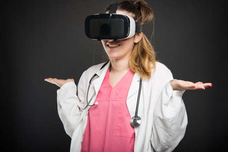 Female doctor wearing virtual reality glasses and gesturing  not knowing on black backgroundの写真素材