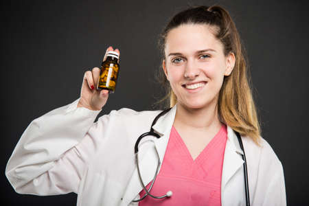 Attractive female doctor holding bottle of pills and smiling on black backgroundの写真素材