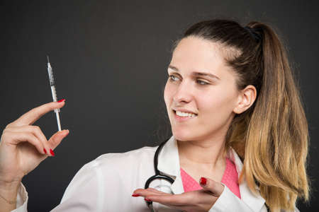 Side view of female doctor showing syringe and smiling on black backgroundの写真素材