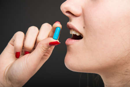 Close-up of female doctor mouth taking one pill  on black backgroundの写真素材