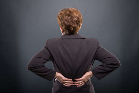 Business senior lady holding  her back like hurting on black background with copyspace advertising areaの写真素材