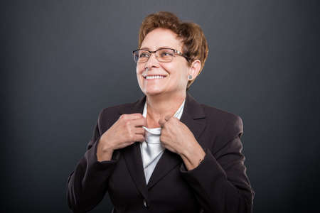 Business senior lady posing arranging her shirt and smiling on black backgroundの写真素材