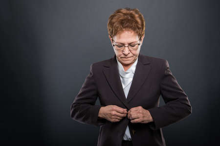 Business senior lady posing buttoning her jacket on black background with copypsace advertising areaの写真素材