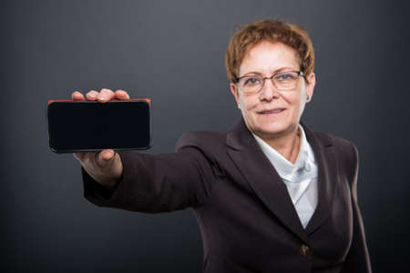 Selective focus of business senior lady showing smartphone on black background
