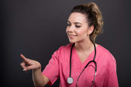 Portrait of beautiful young doctor using touchscreen with index finger on black backgroundの写真素材