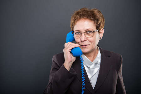 Business senior lady speaking at big blue telephone receiver on black background with copyspace...