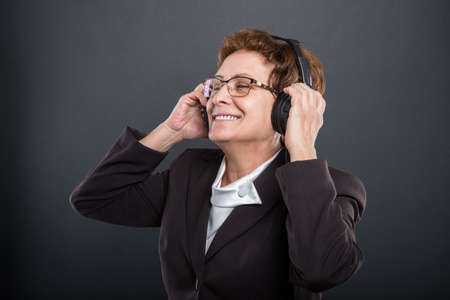 Portrait of business senior enjoying listening to headphones on black background
