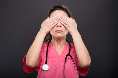 Portrait of lady doctor covering eyes like not seeing or blind concept on black backgroundの写真素材