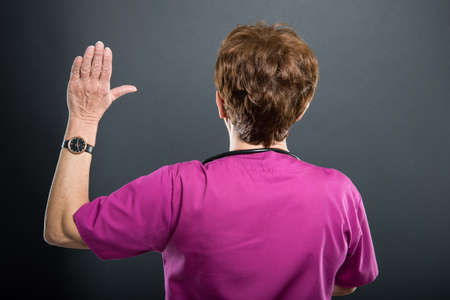 Back view of senior lady doctor taking oath on black backgroundの写真素材