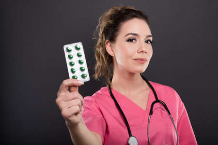 Portrait of beautiful young doctor holding two blister of pills on black background with copypsace advertising areaの写真素材
