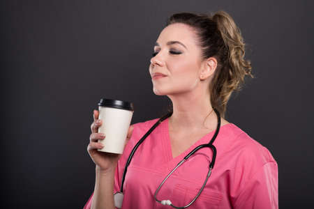 Side view of beautiful young doctor holding takeaway coffee and smiling on black background with copypsace advertising areaの写真素材