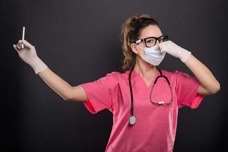 Portrait of attractive lady doctor holding cigarette gesturing bad smell like no smoking concept on black backgroundの写真素材