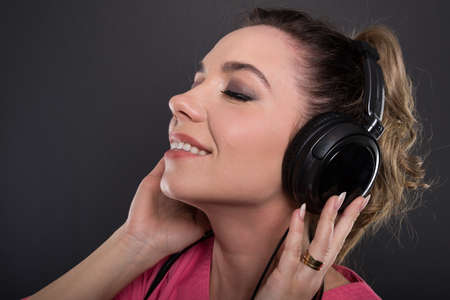 Close-up of beautiful young doctor listening to headphones and smiling on black backgroundの写真素材