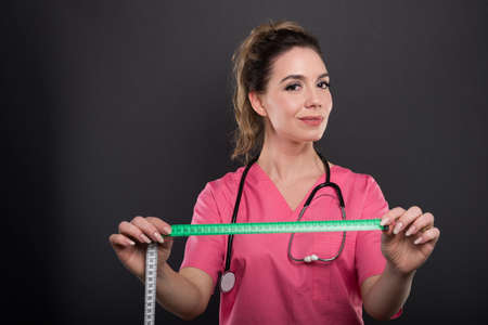 Portrait of attractive lady doctor holding measuring tape on black background with copypsace advertising areaの写真素材
