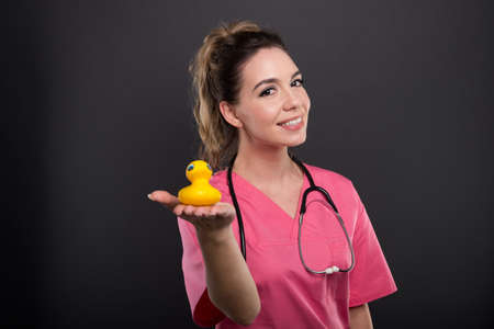Portrait of attractive lady doctor showing small bath duck on black background with copypsace advertising areaの写真素材
