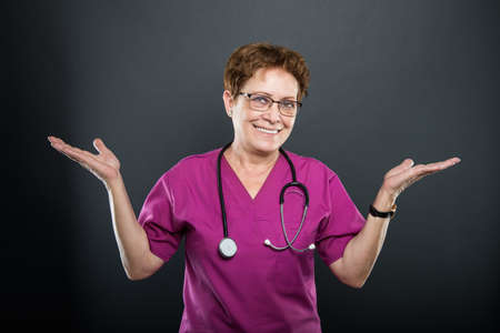 Portrait of senior lady doctor showing copyspace area with both hands and smiling on black backgroundの写真素材