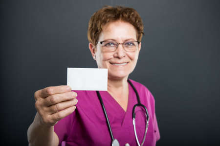 Selective focus of senior lady doctor showing business card and smiling on black backgroundの写真素材