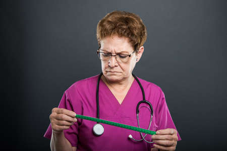 Portrait of senior lady doctor looking at measuring tape on black backgroundの写真素材