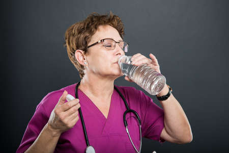Portrait of senior lady doctor drinking water from the bottle on black backgroundの写真素材