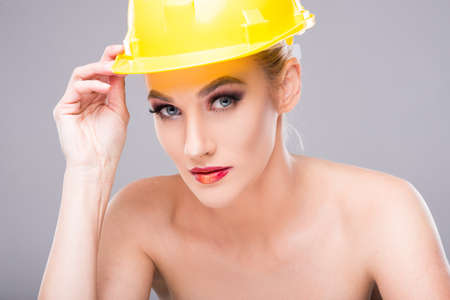 Beautiful model posing wearing make-up and yellow hardhat on grey backgroundの写真素材
