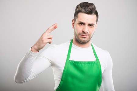 Attractive supermarket employer with fingers crossed looking serious on white backgroundの写真素材