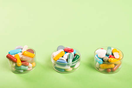Three cups of colorful pills and tablets on green background with copyspace advertising areaの写真素材
