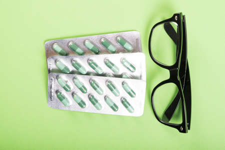 Blister of tablets and pair of black glasses on green backgroundの写真素材