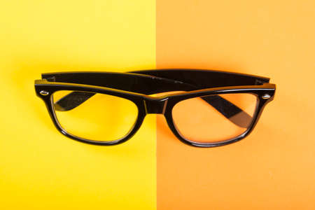 One pair of black glasses on yellow and orange backgroundの写真素材