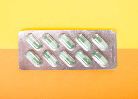 One blister of green tablets on yellow and orange backgroundの写真素材