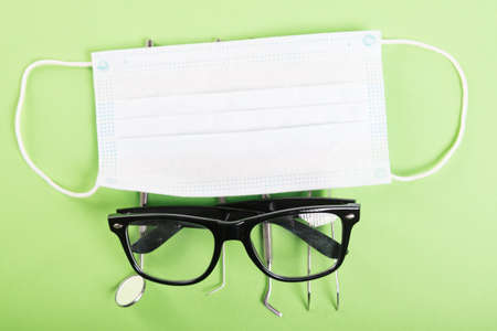 Dentistry set of tools with glasses and face mask on green background