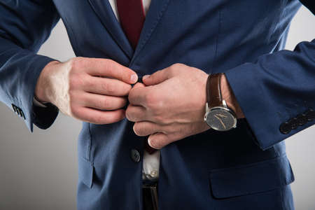 Close-up of business man wearing suit buttoning his jacket on gray backgroundの写真素材