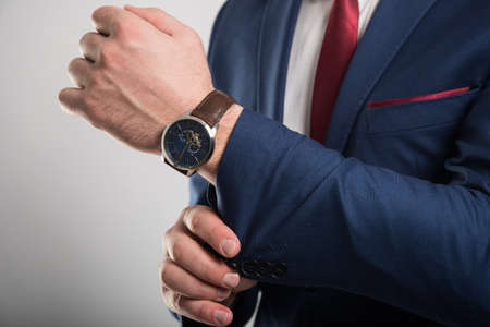 Close-up of business man wearing suit arranging jacket sleeve on gray backgroundの写真素材